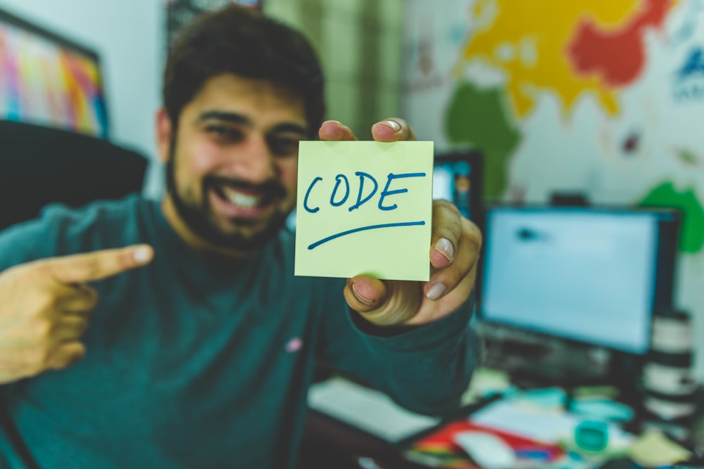 Homem sorridente mostrando nota adesiva com ilustração de código