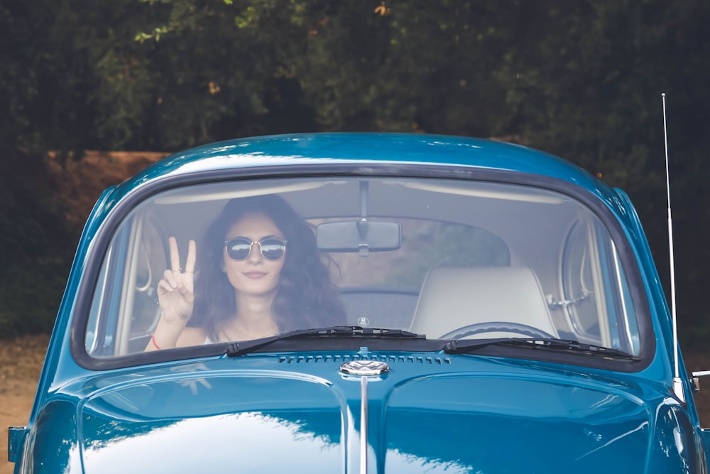 woman sitting in passengers seat of blue Volkswagen Beetle and performing peace sign