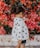 girl in black and white polka-dot long-sleeved blouse and blue shorts standing beside red petaled flowers during daytime