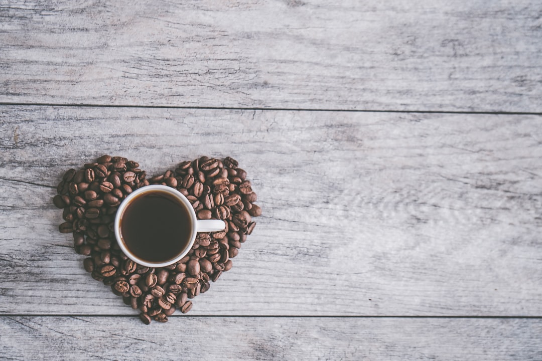 coffee filled white ceramic mug beside brown coffee beans on beige wooden surface,