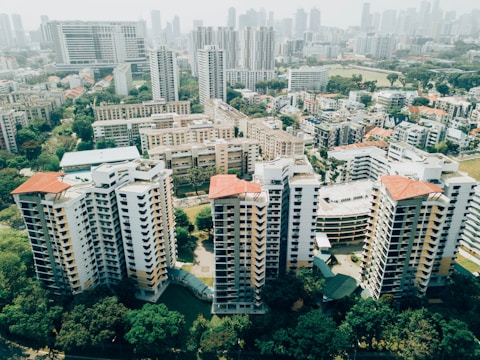 Aerial view of a cityscape featuring multiple high-rise apartment buildings surrounded by lush greenery. The skyline in the background is filled with numerous skyscrapers under a hazy sky.