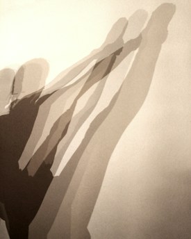 Multiple elongated shadows of a person in a dynamic stretching pose appear on a plain background. The shadows overlap and create a layered effect, suggesting movement and depth.