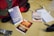 A collection of items is arranged on a light-colored surface, including a red and gray backpack, a blue pamphlet titled 'An Intelligent Faith?', an orange pamphlet titled 'Evolution Impossible', and another with the title 'The End of the World?'. Additionally, there is a silver wristwatch, a set of car keys, a notepad with a pen, and white earphones.