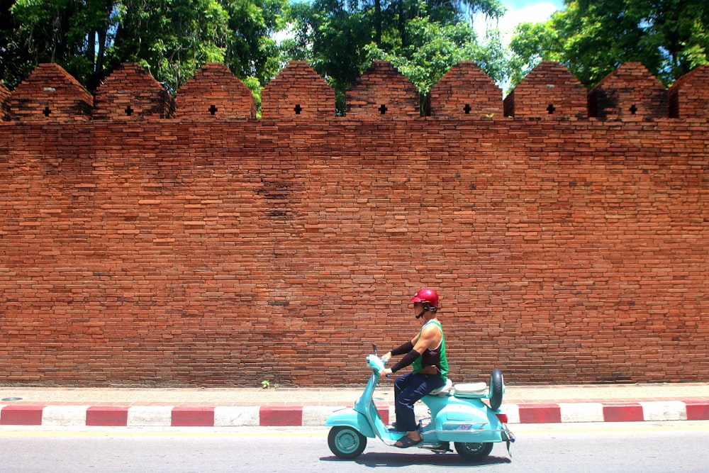 man riding teal motor scooter on road during daytime