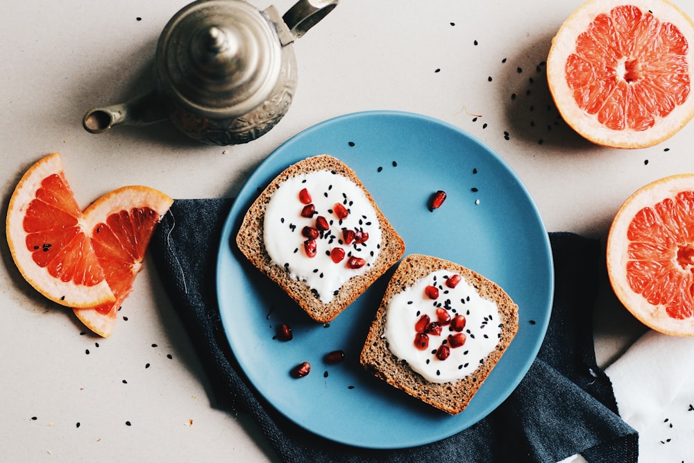 two baked breads with white mayonnaise and red fruits on top in round blue ceramic plate