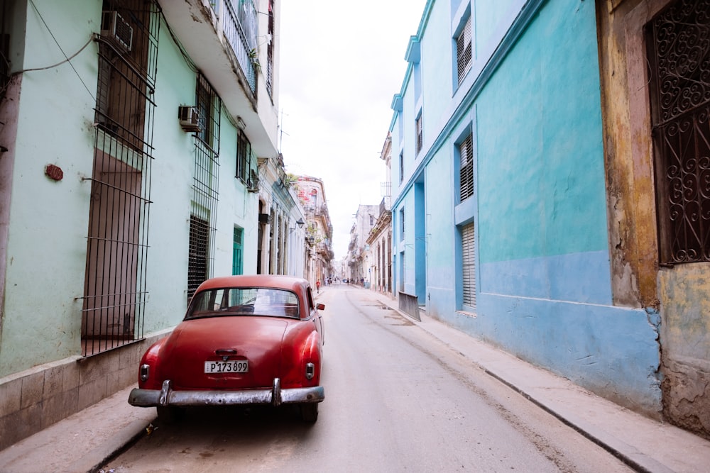 classic red vehicle on alley under gray sky during daytime