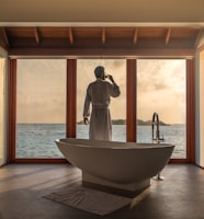 man standing in bathroom with bathtub next to body of water