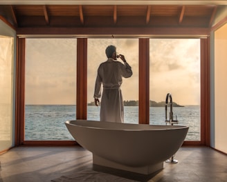 man standing in bathroom with bathtub next to body of water