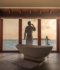 man standing in bathroom with bathtub next to body of water