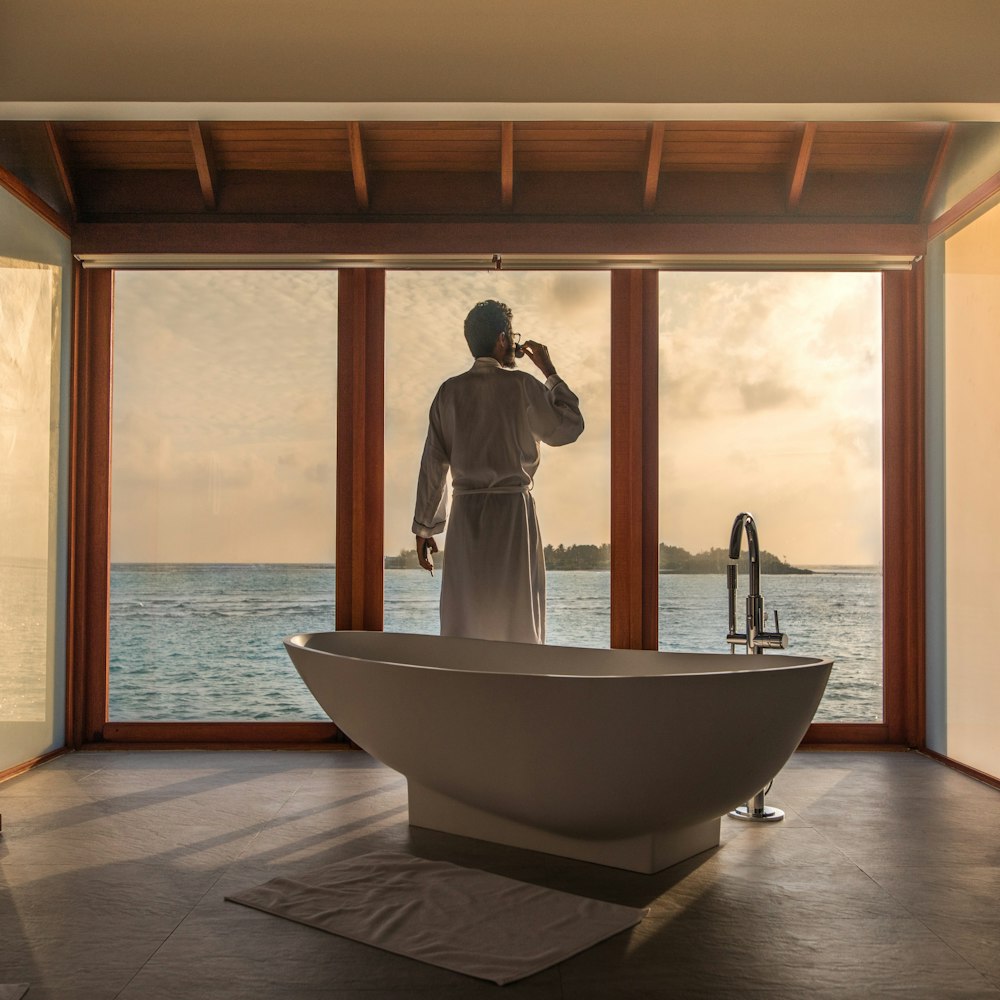 man standing in bathroom with bathtub next to body of water