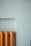 A vibrant orange radiator stands out against a muted light blue wall. The radiator's design features multiple evenly spaced vertical sections, showing a simple yet striking contrast in both color and form.