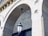 An ornate stone archway with detailed architectural elements. A vintage-style lantern is hanging from the center of the arch. The ceiling has a pattern of small, scattered dark marks against a lighter background. The stonework features decorative moldings and cornices.