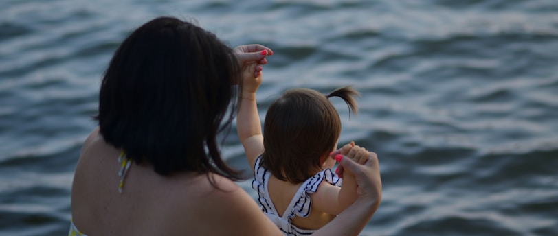 woman holding girl near body of water