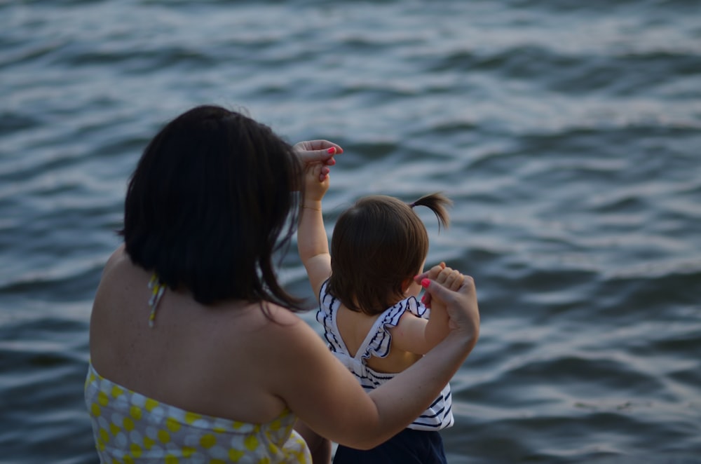 woman holding girl near body of water