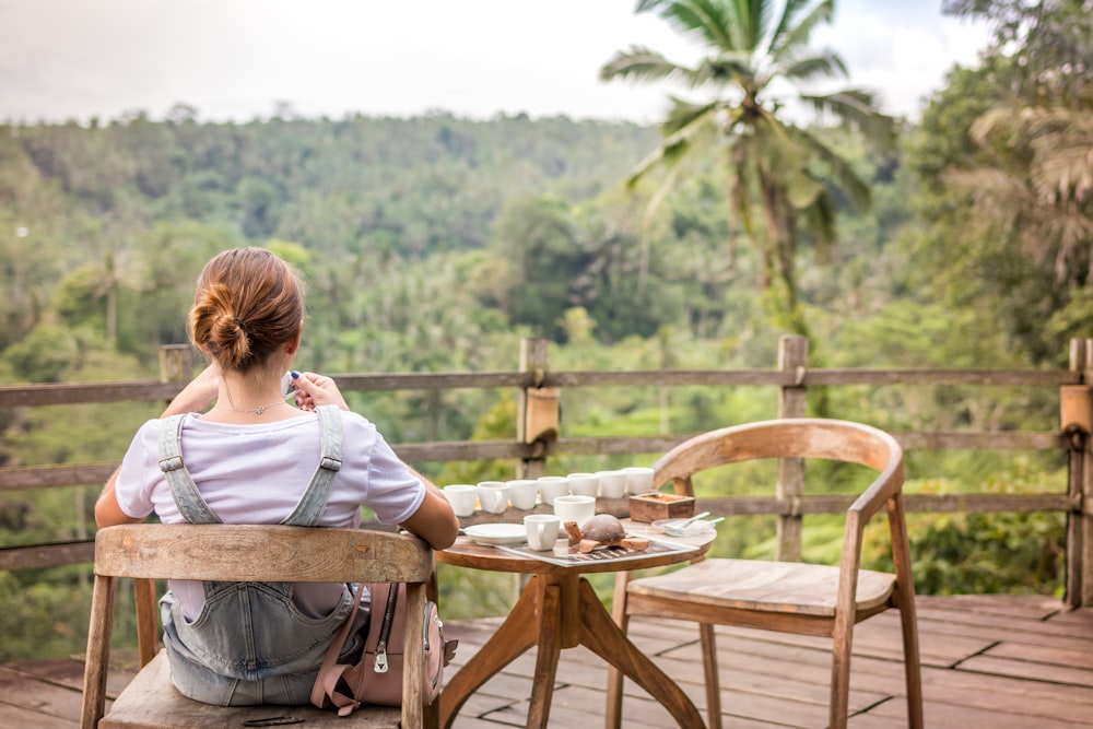 woman sitting on wooden armchair facing forest