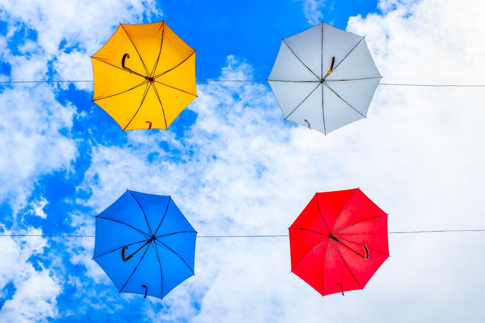 Vier verschiedenfarbige Regenschirme an Kabeln unter bewölktem Himmel aufgehängt