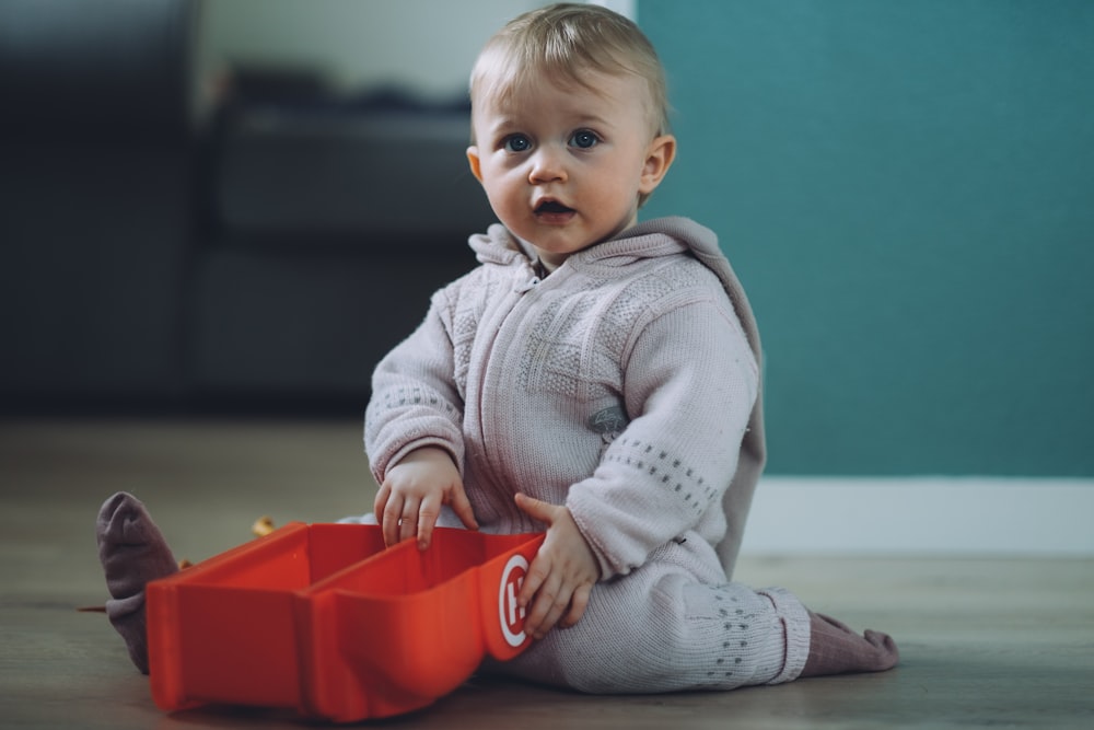 niño pequeño sentado en el suelo mientras sostiene una caja de plástico roja