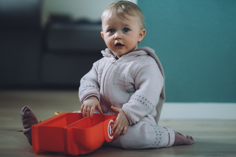 toddler sitting on ground while holding red plastic case