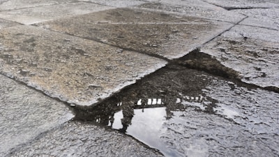 Wet cobblestone pavement with a puddle reflecting part of a building or structure, showing intricate, weathered textures on the stones.