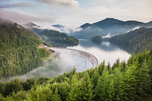 A sleek dam structure blending into a misty mountain river landscape at dawn.