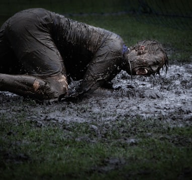 man lying on green grass soaked with mud