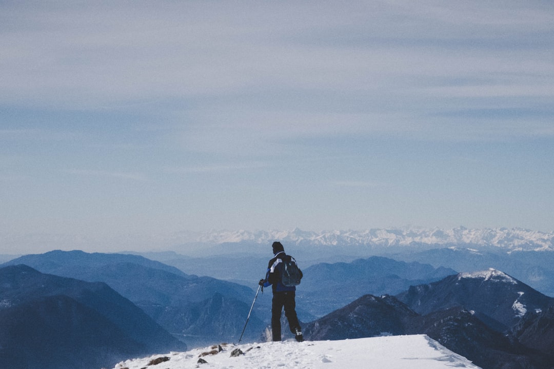 person standing black backpack standing on peak at daytime