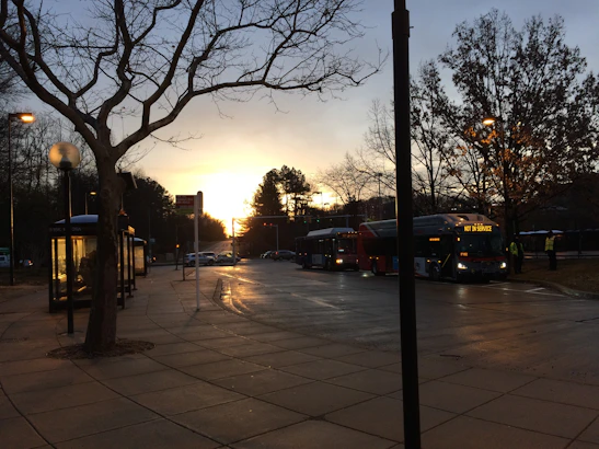 A modern bus departing from a busy northern bus terminal at sunset.