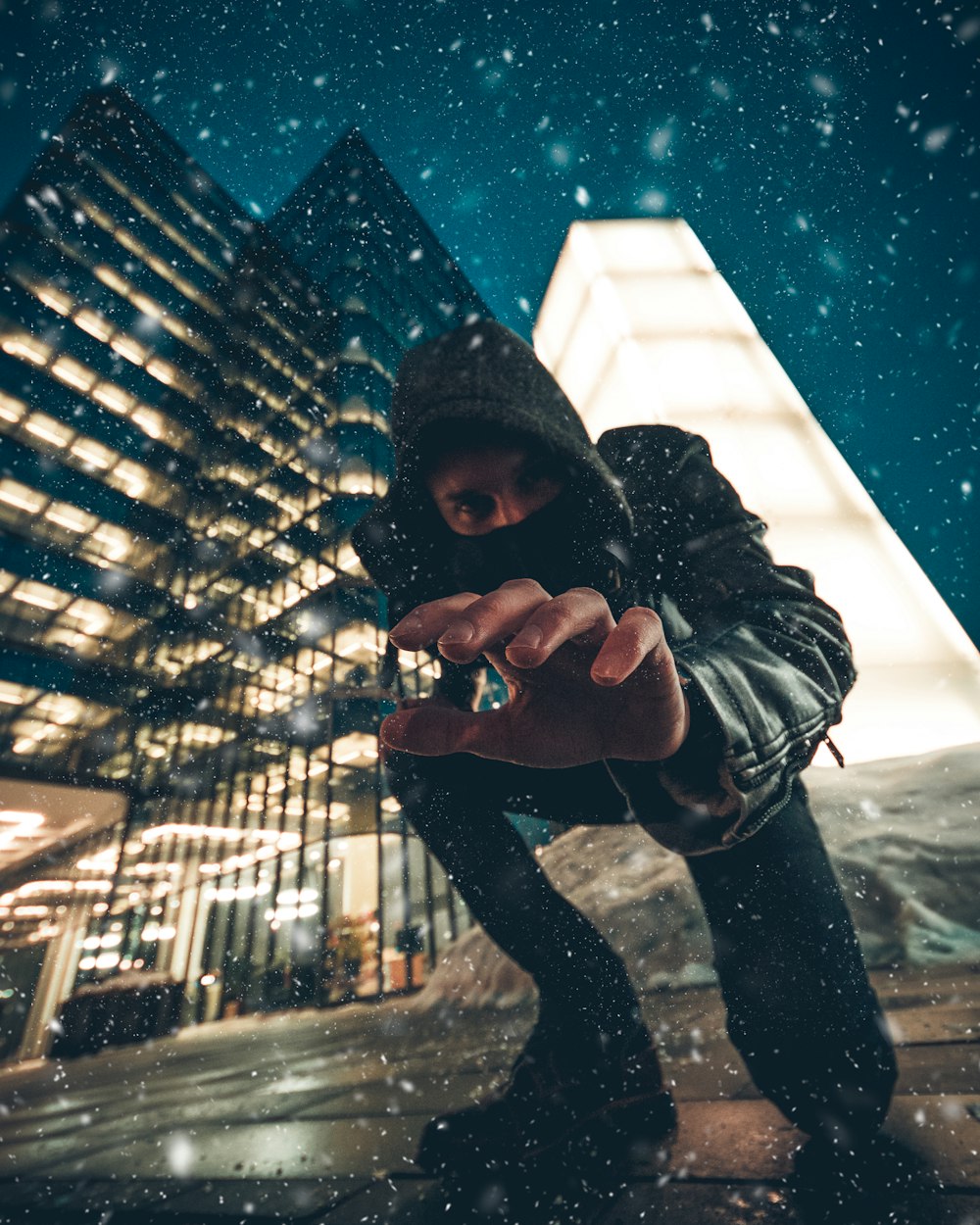 close-up photography of man kneeling on ground front of gray high-rise building during snow weather