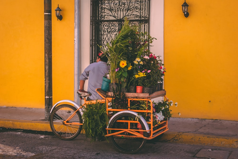 hombre de pie cerca del triciclo amarillo con macetas de flores