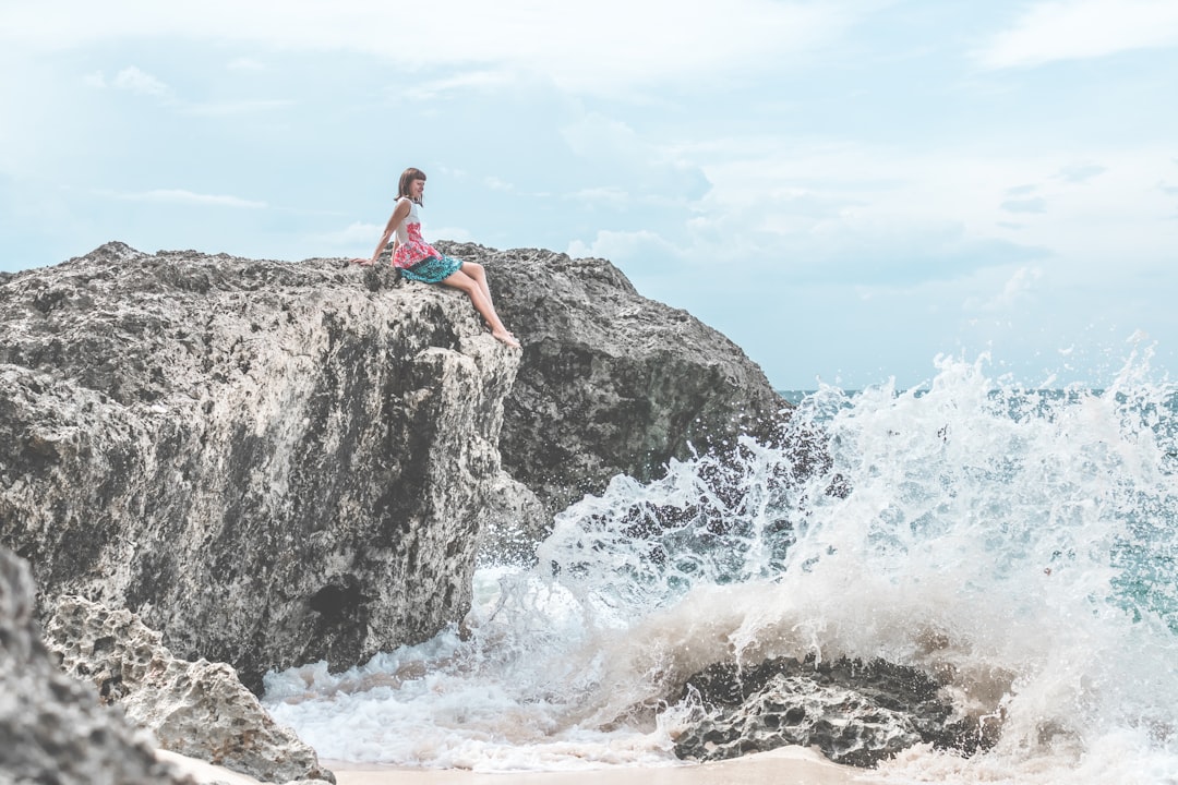 woman in pink top sitting on gray cliff