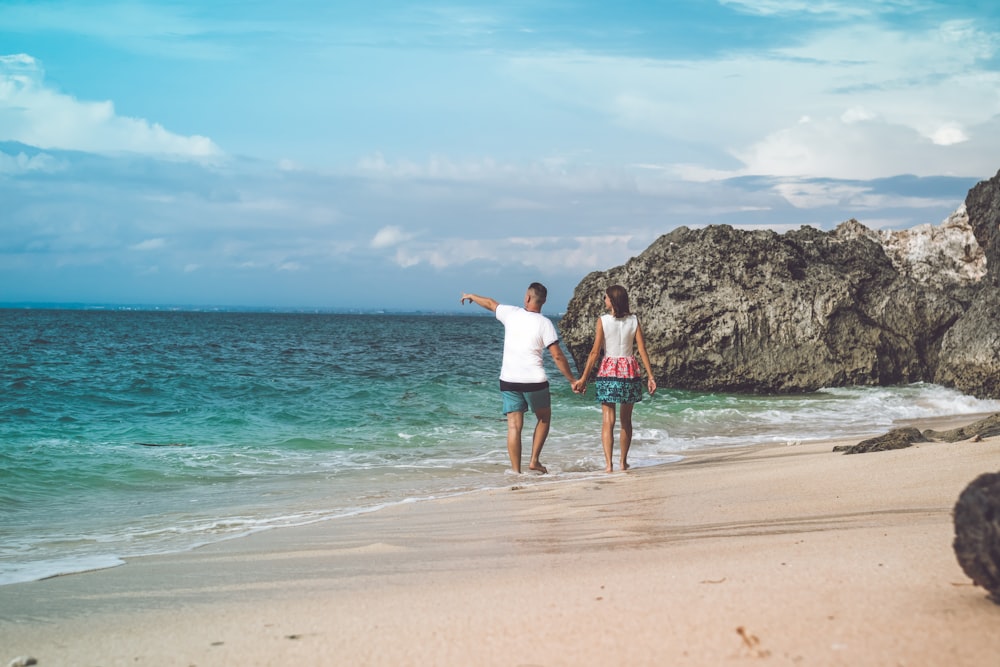 man and woman walking on seashore while holding hands during daytime