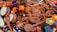 A collection of wooden spoons scattered with vibrant wooden toys and tambourines intermixed. The toys are brightly colored, featuring elements like an orange animal, drumheads, and decorative flowers.
