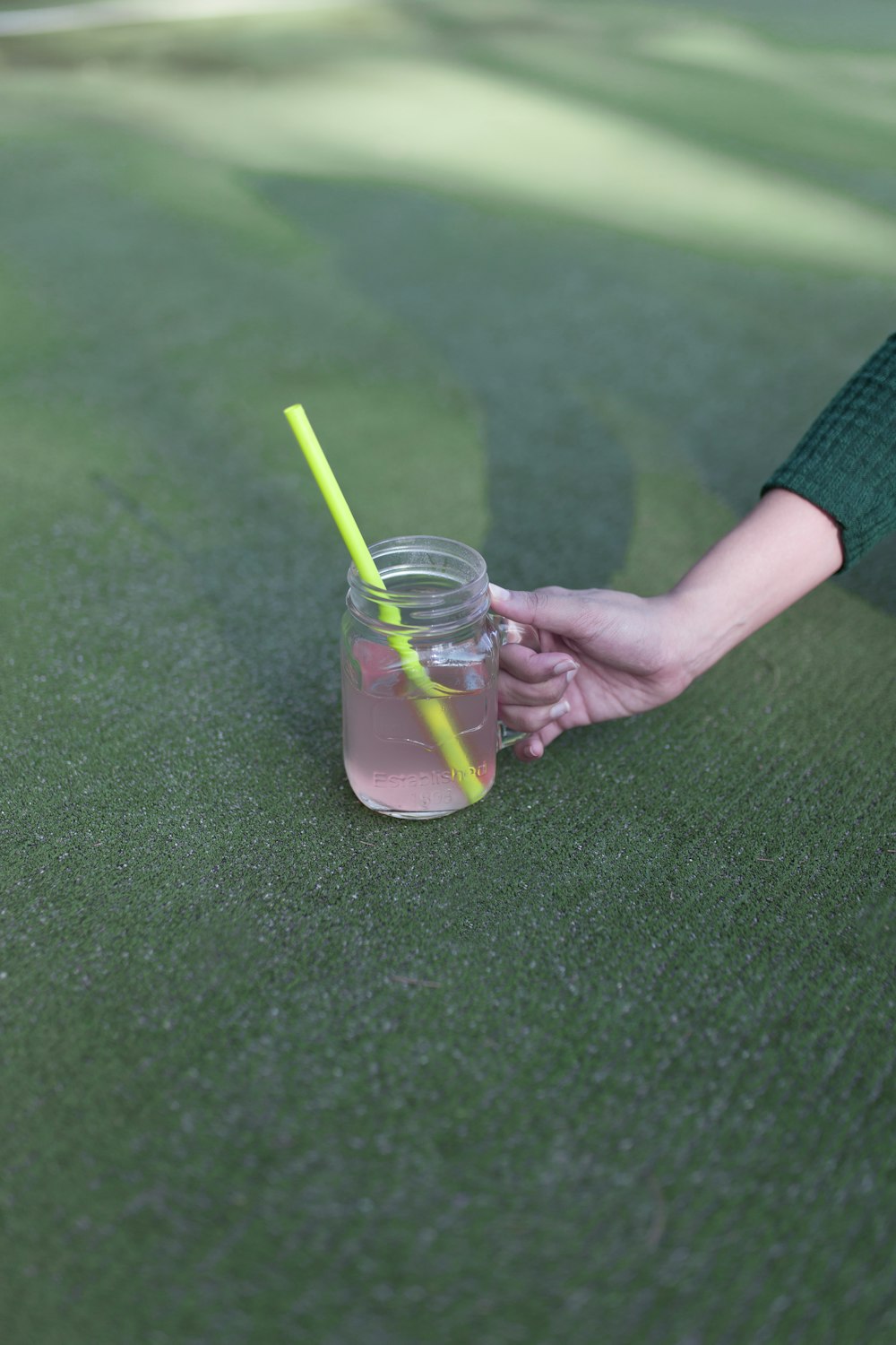 person holding mason jar filled beverage with straw