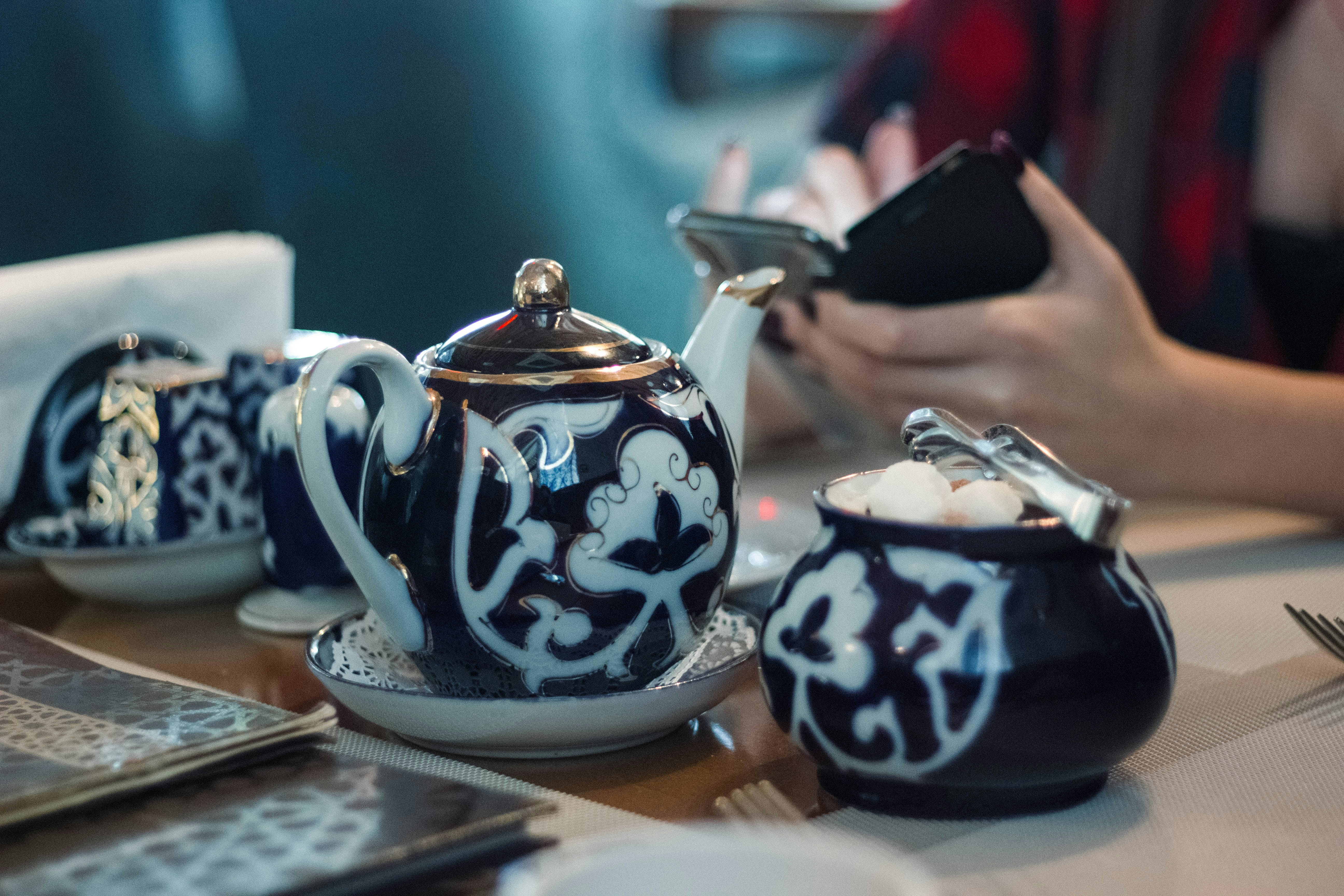 person sitting in front white and black ceramic tea set pot of gold teams background