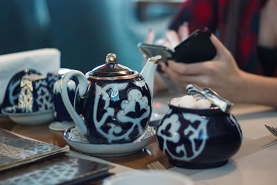 person sitting in front white and black ceramic tea set pot of gold google meet background