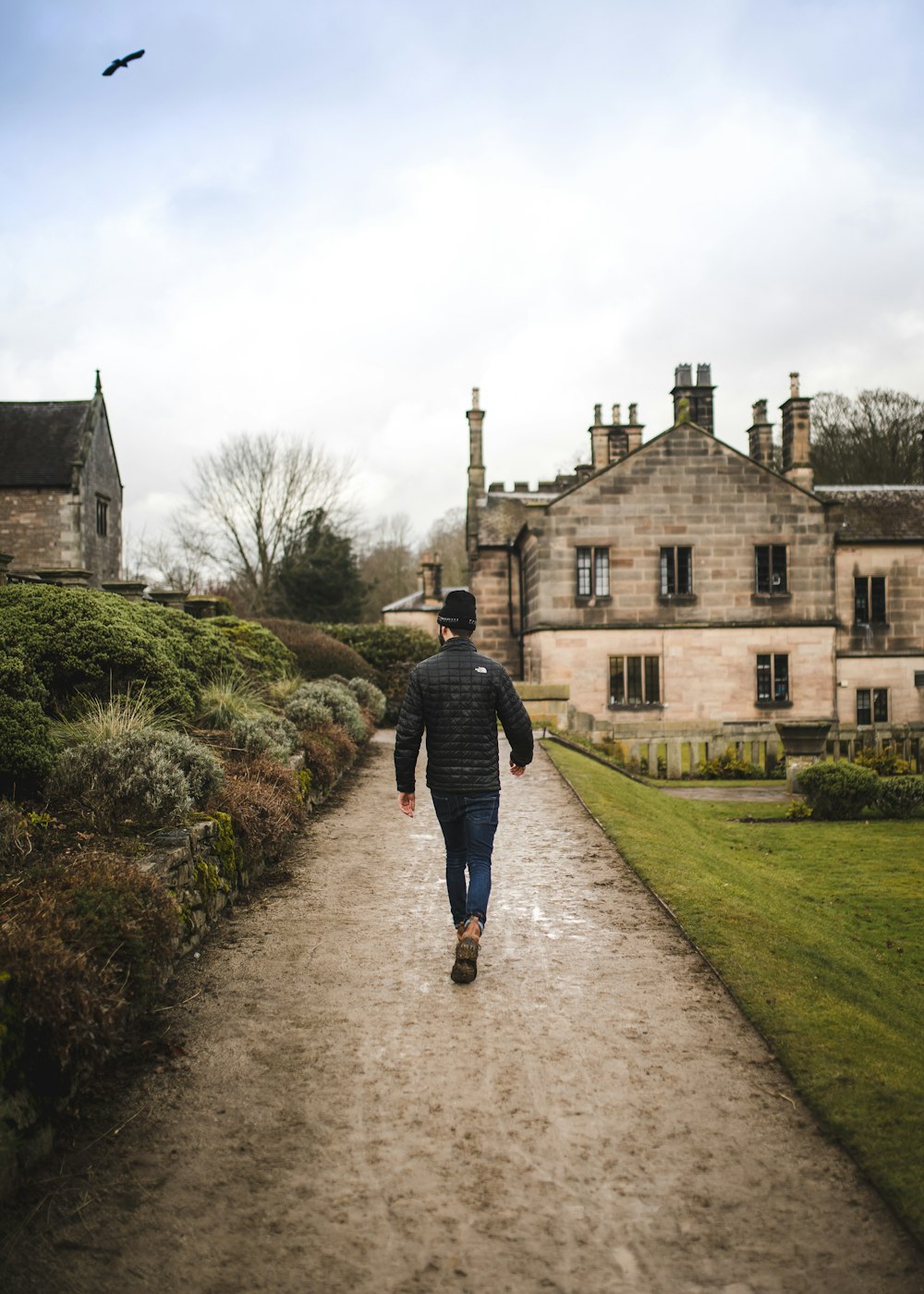 man walking on dirt road near brick house during daytime