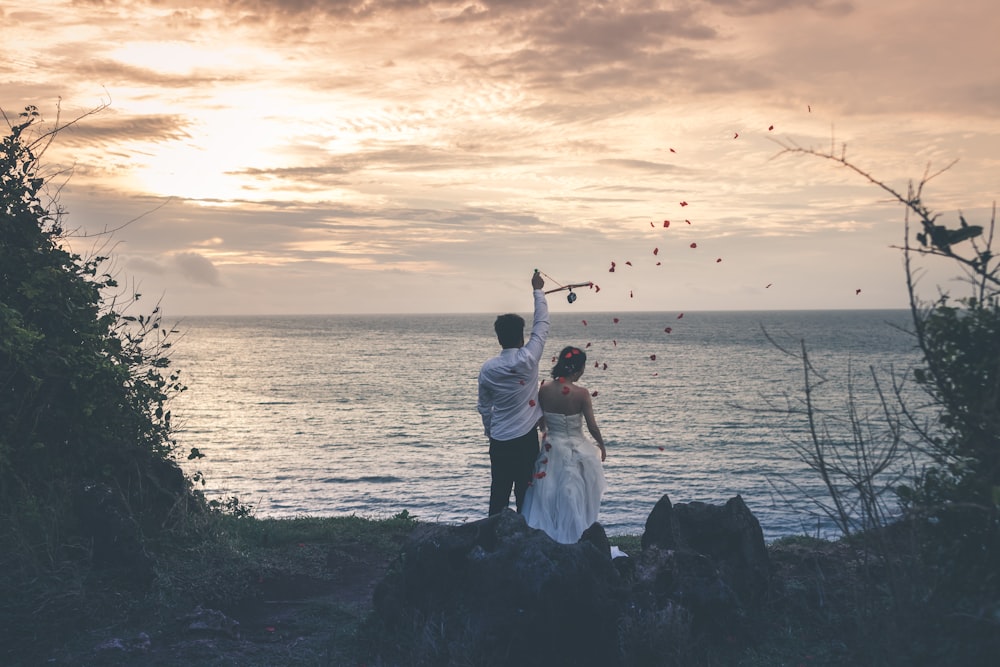 bride and groom standing in front of water body