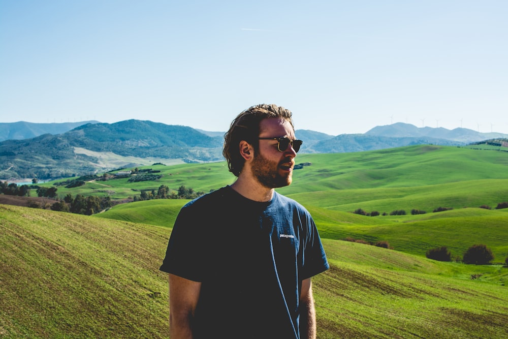 man wearing black crew-neck t-shirt standing near hill at daytime