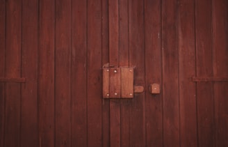 A wooden door with vertical planks and a large central latch bolted securely. The texture of the wood is rough, with visible grain and a dark brown finish.