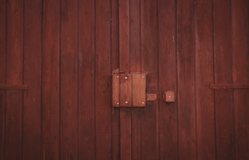 A wooden door with vertical planks and a large central latch bolted securely. The texture of the wood is rough, with visible grain and a dark brown finish.