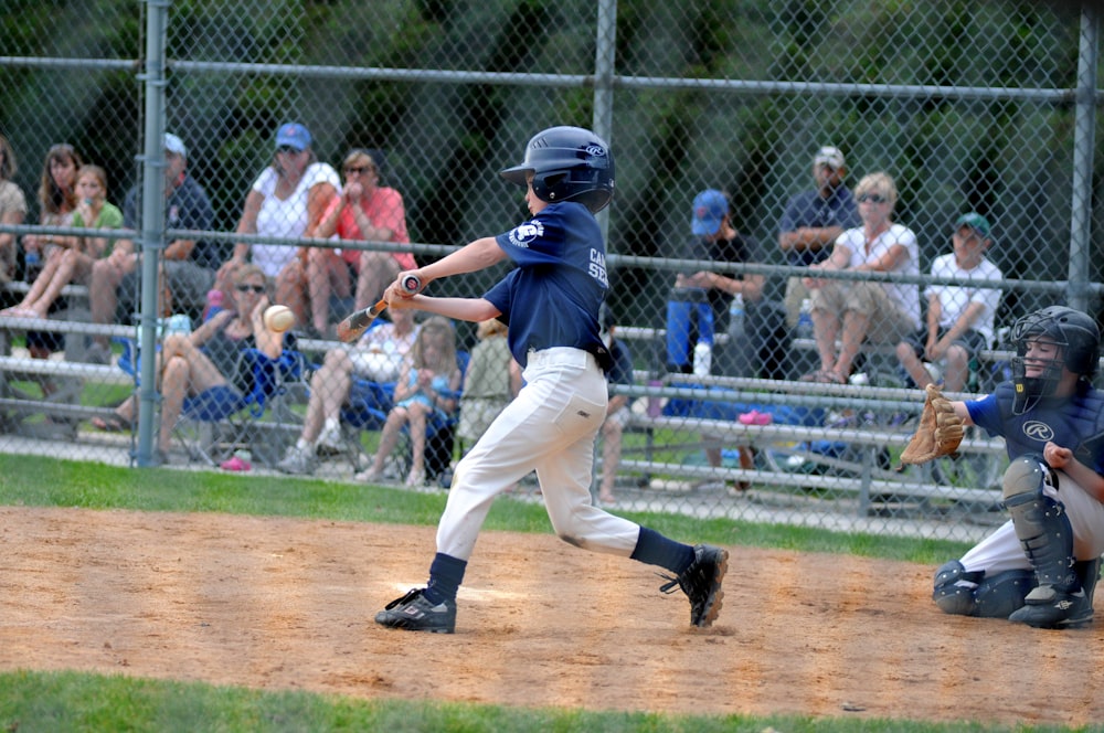 Junge schlägt Baseball in der Nähe von Fänger neben grauem Zaun