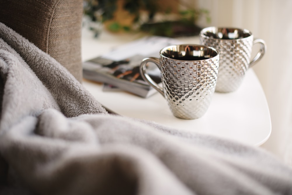 two silver mugs on white side table