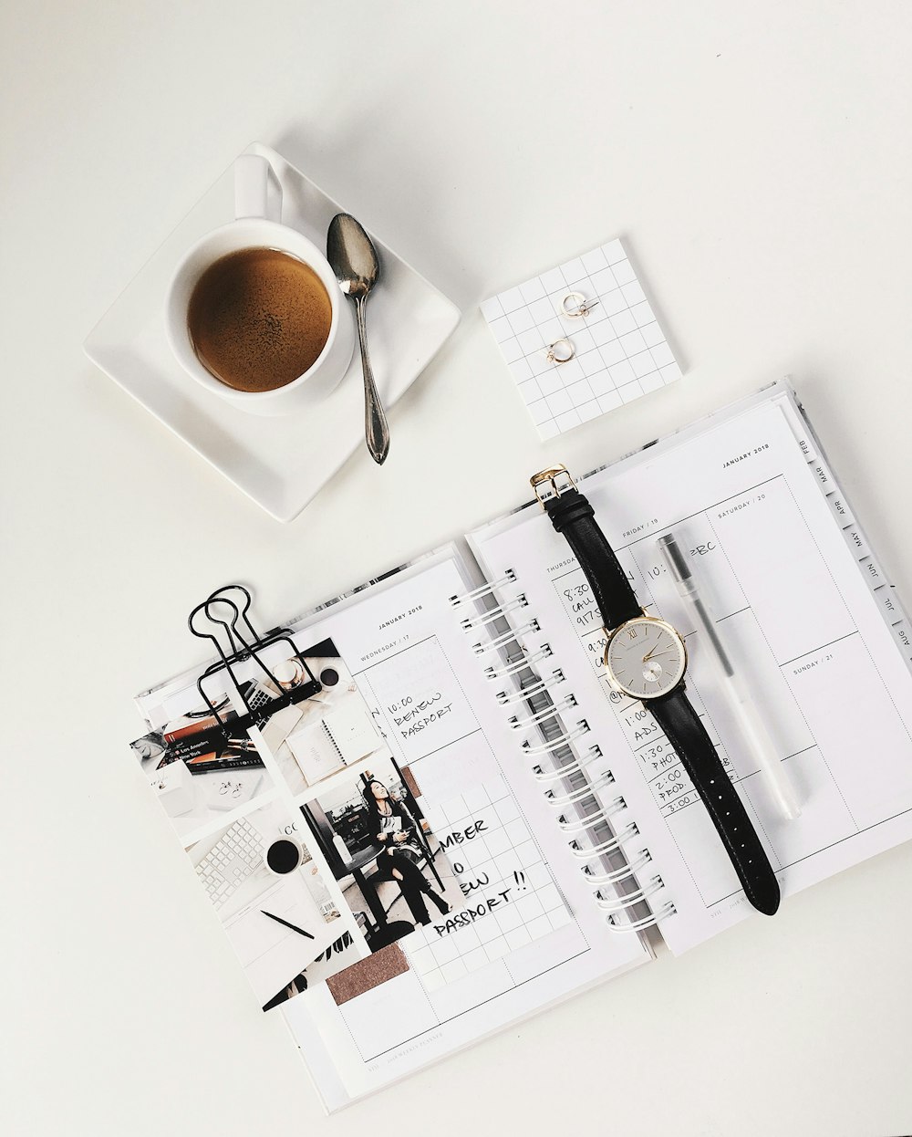 analog watch on top of book beside white ceramic teacup with teaspoon