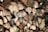 A stack of cut firewood with visible tree rings and textures. The logs are arranged tightly together, showcasing their brown and beige hues with darker shadowed areas in between.