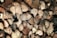A stack of cut firewood with visible tree rings and textures. The logs are arranged tightly together, showcasing their brown and beige hues with darker shadowed areas in between.
