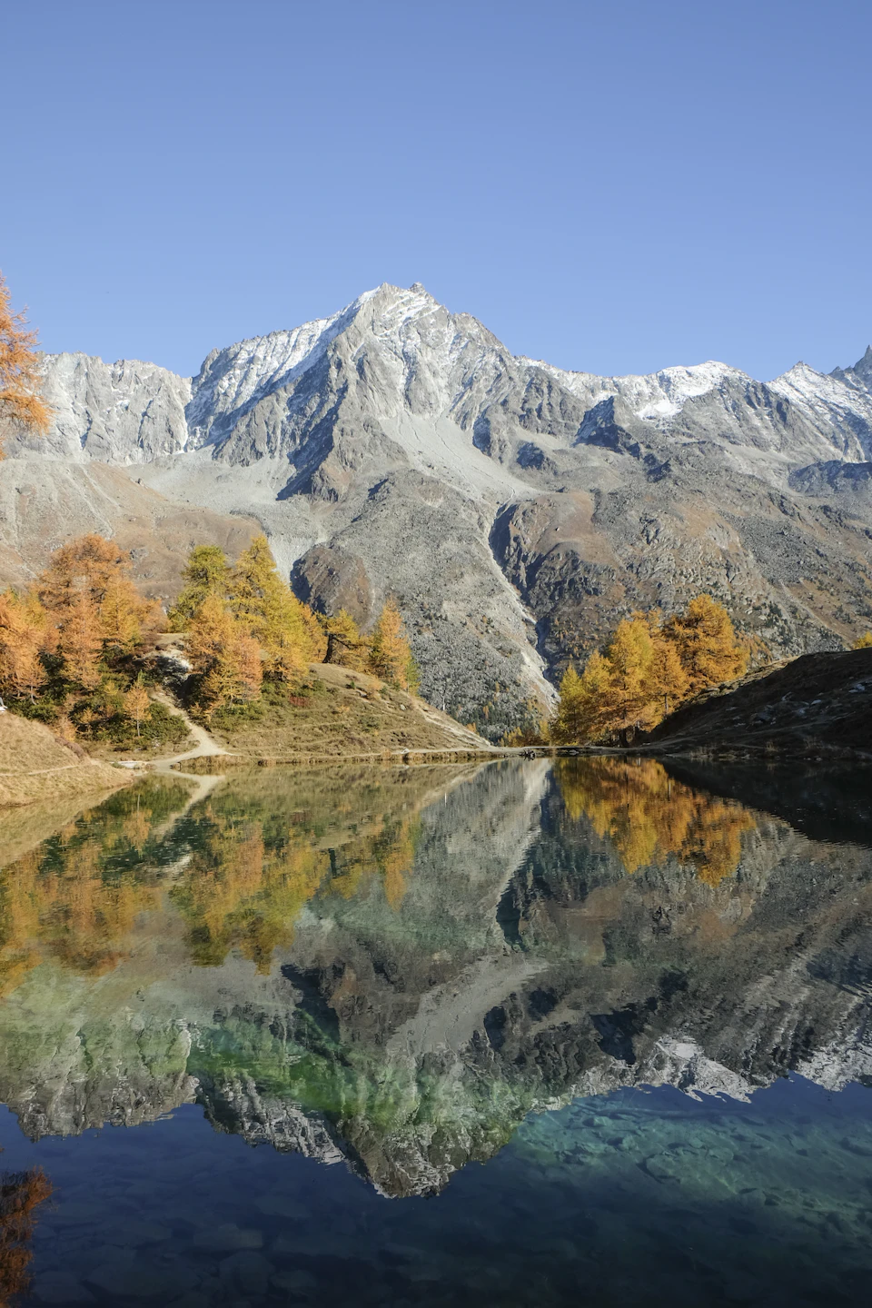 Serene mountain lake surrounded by lush green trees and snow-capped mountain peaks reflected perfectly