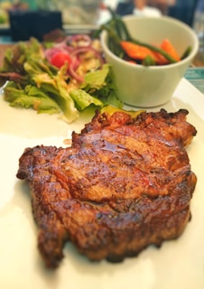 Grilled steak served with a side of colorful seasonal vegetables on a dark plate.
