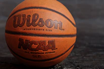 A close-up of a basketball spinning on a player's fingertip, with the academy’s orange and white colors in the background.