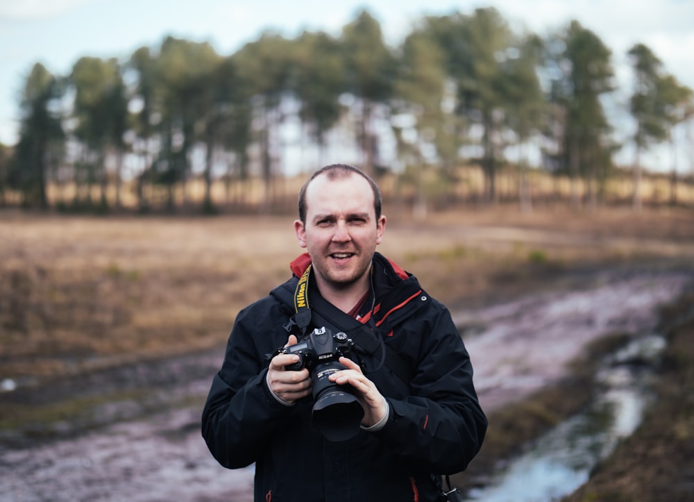 man holding black Nikon DLSR camera while standing on road during daytime