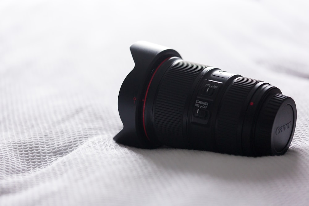 black Canon camera zoom lens on top of white bed sheet